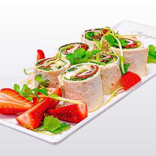 Bilde av wraps fylt med kremost, serranoskinke, soltørket tomat og sprø grønn salat, rullet sammen og skåret i delikate serveringsbiter. En smakfull tapasrett med balanserte smaker av salt, søtt og kremet.