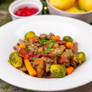 Bilde av viltgryte med mør strimlet viltkjøtt, løk, skogsopp og kremet fløtesaus, servert med baconsautert rosenkål, tyttebær og poteter.