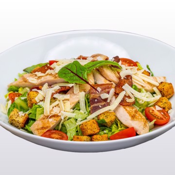 Bilde av cæsar salat med sprø romano- og hjertesalat, knasende krutonger, revet parmesan, saftig kyllingbryst og sprøstekt bacon. Serveres med kremet Cæsardressing, kuvertbrød og smør. En klassisk og smakfull salat.