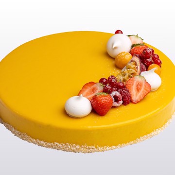 Mangomoussekake med hvit sjokoladeglasur, nøttebunn og kokos – pyntet med bær og marengs.