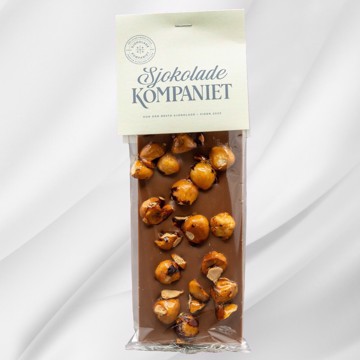 Bilde av Karamellisert Hasselnøtt sjokoladeplate fra Sjokoladekompaniet, laget med fyldig melkesjokolade og søt karamellsjokolade, kombinert med hele, karamelliserte hasselnøtter. En perfekt balanse mellom sprø nøtter og kremet sjokolade for en harmonisk smaksopplevelse.